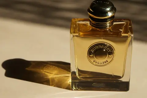 Złota butelka perfum Burberry Goddess, lśniąca w świetle, z wytłoczonym logo.