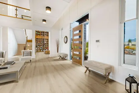 Amplio vestíbulo con suelo de vinilo autoportante de madera clara, puerta principal de madera, escaleras y estanterías.