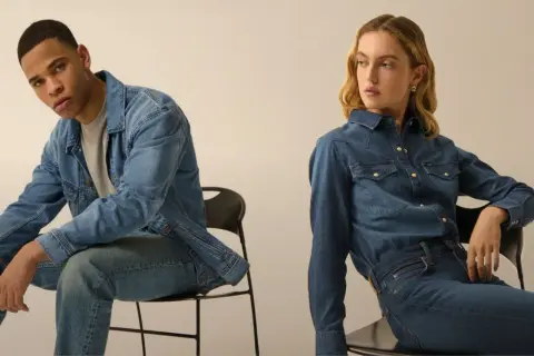 Coppia in total look denim. Lui con giacca e jeans, lei con camicia e jeans, entrambi con un fit che si stringe verso il basso, il tapered fit significato.