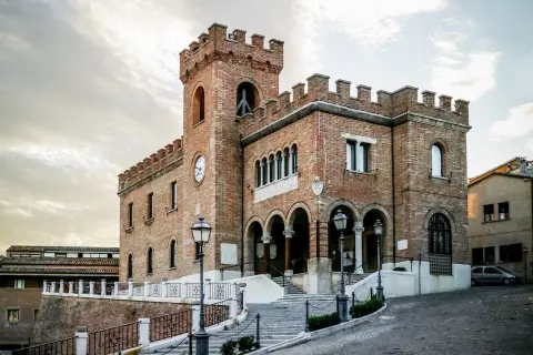 Edificio in mattoni rossi con torre dell'orologio e merlature, un esempio di cosa vedere a Mondolfo.