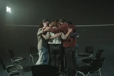 Grupa ludzi w kręgu, wspierająca się nawzajem. To obraz grupy wsparcia po stracie bliskiej osoby, gdzie dzielenie się bólem i nadzieją jest kluczowe.