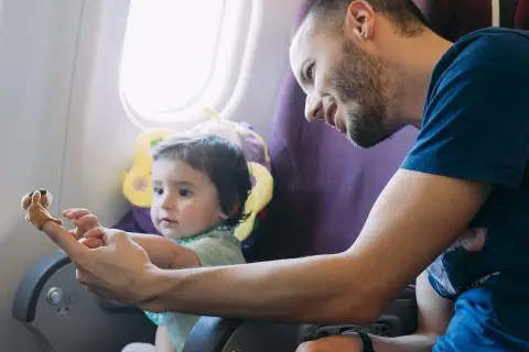 Tata bawi dziecko paluszkową zabawką, jednym z gadżetów do samolotu dla dzieci.