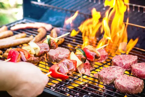 Brochettes de viande et légumes, saucisses et steaks sur un barbecue au barbecue, avec des flammes vives.