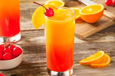 Cóctel refrescante con capas de granadina y naranja, adornado con una cereza y rodajas de naranja.