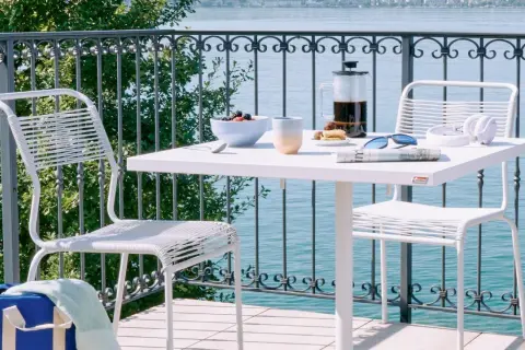 Idee per arredare balcone piccolo: tavolino bianco con caffè, frutta e sedie moderne, vista lago.
