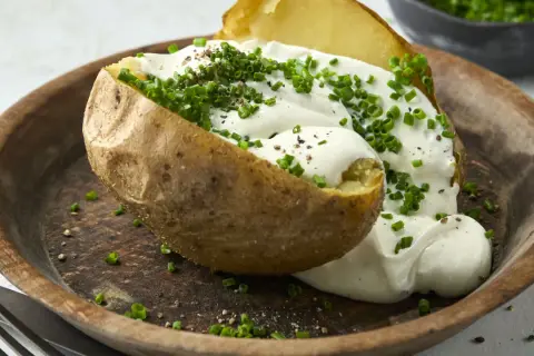 Ofenkartoffel mit reichlich saurer Sahne und Schnittlauch bestreut, serviert auf einem rustikalen Holzteller.