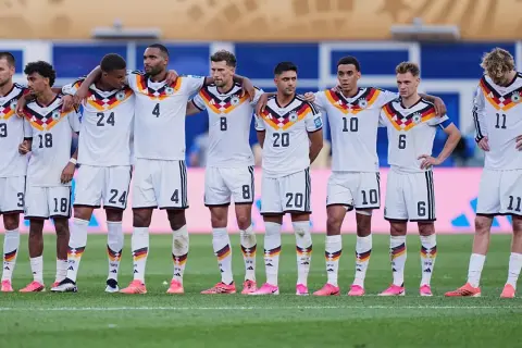 Drużyna Niemcy FC w białych strojach, z numerami na koszulkach, stoi na murawie.