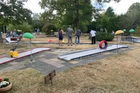 Familien spielen Minigolf Gummersbach. Bunte Bahnen mit Hindernissen wie einem roten Reifen laden zum Spiel ein.
