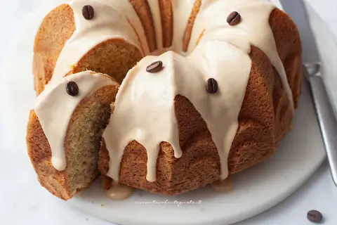 Una deliziosa torta al caffè, con glassa chiara e chicchi di caffè come decorazione. Una fetta è stata tagliata, rivelando l'interno soffice.