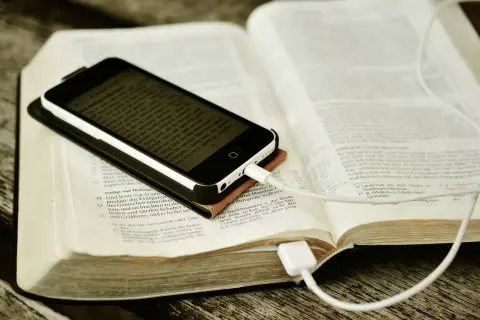 Nowoczesna biblia na co dzień: smartfon z tekstem biblijnym leży na otwartej księdze, podłączony do ładowania.