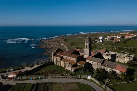 Monasterio de Santa María de Oia, con su torre campanario y tejados rojizos, se alza majestuoso junto al mar Cantábrico.