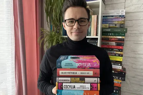 Mężczyzna trzyma stos książek, wśród nich "Reguły gry" Colsona Whiteheada. Czytelnik szuka informacji o lee child jack reacher kolejność.