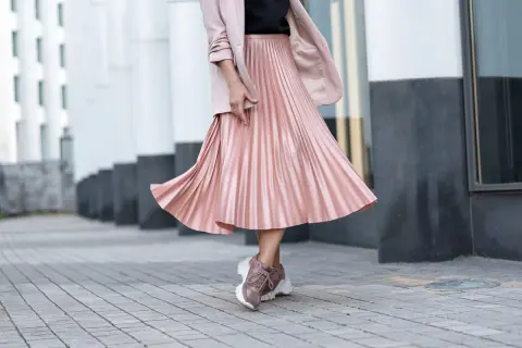 Gonna plissettata rosa cipria, un outfit inverno chic con blazer e sneakers.