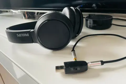 Czarne słuchawki Philips podłączone do adaptera Bluetooth TX/RX na białym blacie.