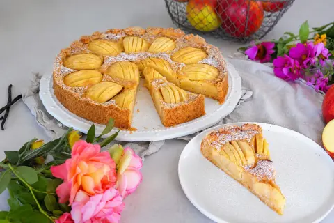 Ein sensationelles Apfeltarte-Rezept: goldbrauner Boden, saftige Äpfel, Puderzucker. Daneben eine Rose und Äpfel im Korb.