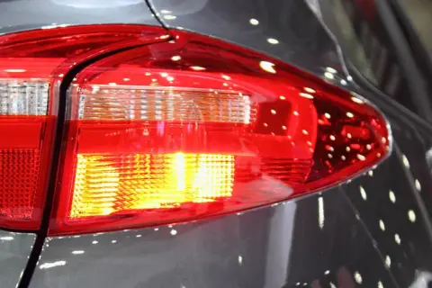 Rücklicht eines Autos, der Blinker blinkt schnell. Reflektionen auf dem grauen Lack.