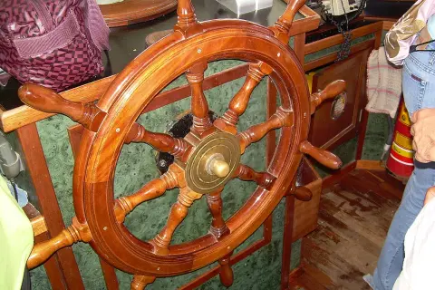 Il timone, come si chiama il volante della nave, è di legno lucido, pronto a guidare.