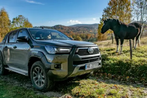 Toyota Hilux GR Sport na tle jesiennych wzgórz, obok stoi koń.