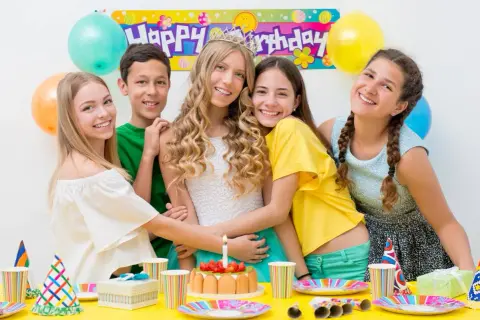 Uśmiechnięci nastolatkowie świętują urodziny przy stole pełnym balonów i tortu. W tle baner "Happy Birthday". Idealne konkursy zabawy na 50 urodziny!