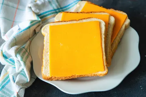 Gotowe do zrobienia pyszne tosty z airfryer. Trzy kromki chleba z serem cheddar na białym talerzyku.