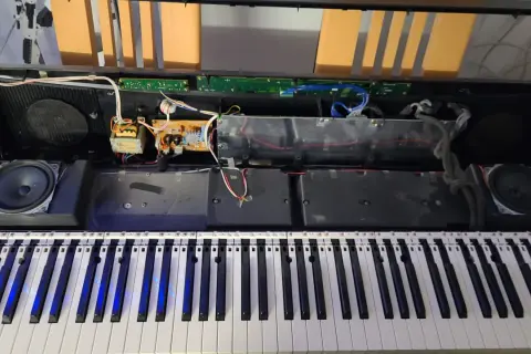 Wnętrze keyboardu podczas naprawy. Widoczne głośniki, płytki drukowane, kable i klawisze.