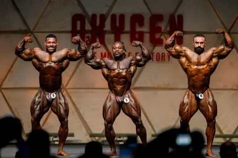 Drei Bodybuilder präsentieren ihre Muskeln auf der Bühne des Mr. Olympia Open.