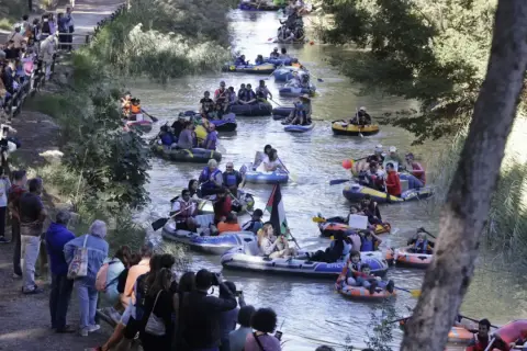 Gente en balsas y kayaks disfrutan de la bajada del canal, rodeados de espectadores en la orilla.