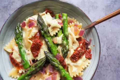 Makaron farfalle z zielonymi szparagami, suszonymi pomidorami i czerwoną cebulą w kremowym sosie.
