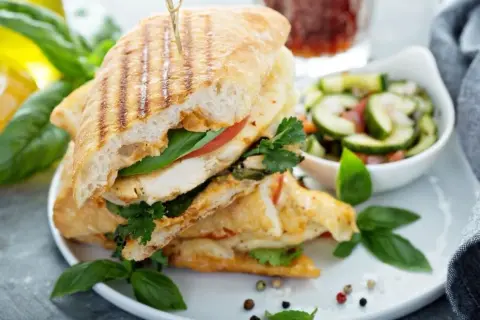 Pyszne panini z kurczakiem, pomidorem i bazylią, podane z sałatką z ogórka. Idealne na szybki lunch.