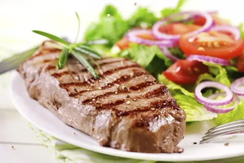 Saftiges Steak mit Grillstreifen, garniert mit Rosmarin, neben einem frischen Salat mit Tomaten und Zwiebeln. Perfekt für die Zubereitung: Steak wie lange im Ofen 100 Grad?