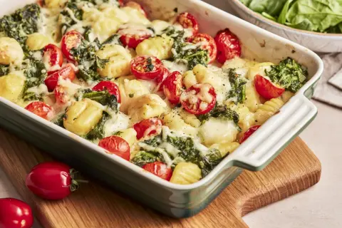 Gnocchi Spinat Auflauf mit Kirschtomaten und geschmolzenem Käse in einer grünen Auflaufform.