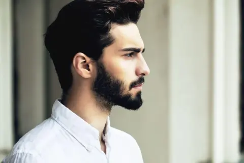 Profil d'un homme avec une barbe haute sur les joues, portant une chemise blanche.