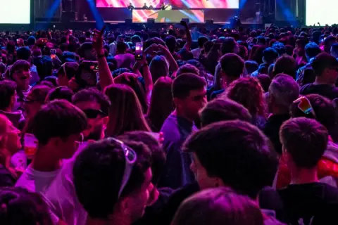 Multitud vibrante en un concierto, luces de neón y un gran cartel de "Espacio Zity" al fondo.