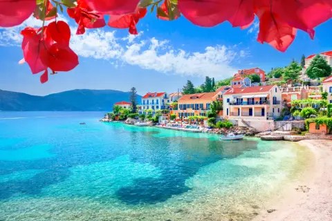 Kefalonia co zobaczyć: malownicza zatoka z turkusową wodą, kolorowe domki na wzgórzu i kwitnące bugenwille. Idealne miejsce na wakacje.