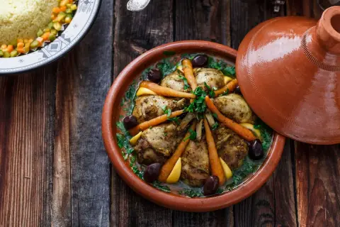 Ein Hähnchen-Tajine mit Karotten, Oliven und Zitrone, serviert in einem traditionellen Tontopf.