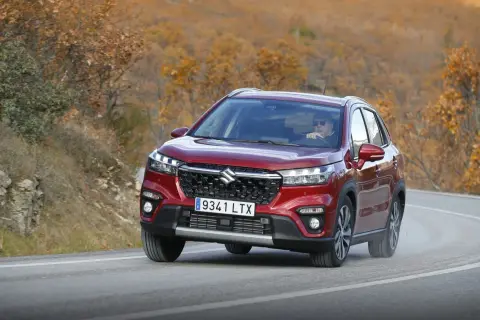 Röd Suzuki S-Cross kör på en kurvig väg i höstlandskap. En man med solglasögon kör bilen under en suzuki s-cross test.