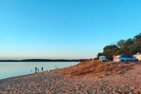 Piękny dzień nad jeziorem Dzierżno Duże. Ludzie kąpią się, a obok zaparkowane samochody i kampery.