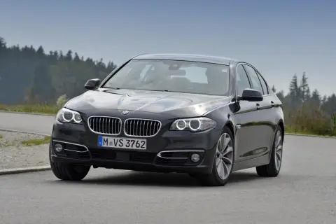 Ciemnoszary sedan BMW F10 na drodze, z widokiem na las. Idealne wymiary dla komfortowej podróży.