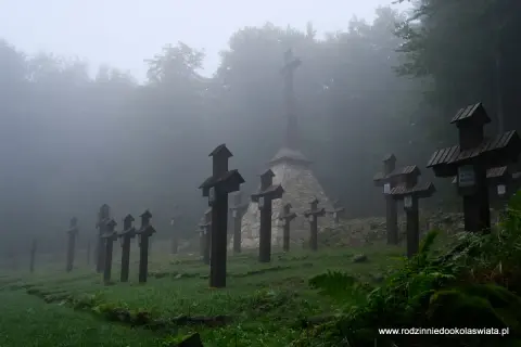 Mglisty poranek na cmentarzu wojennym na Magurze Malastowskiej. Drewniane krzyże stoją w szeregach, a w tle wznosi się monumentalny pomnik.