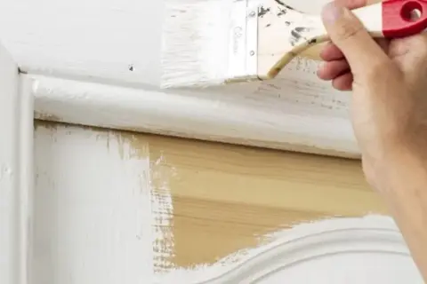 Application de peinture blanche sur un meuble en bois, montrant qu'il est possible de peindre métal sans décaper.