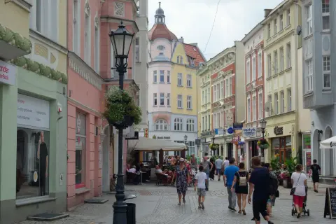 Kolorowa ulica z kamienicami, latarnią i ludźmi spacerującymi po deptaku. Zielona Góra oferuje wiele atrakcji.