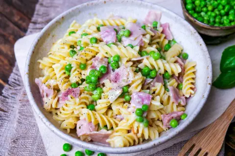 Eine cremige Nudel Schinken Pfanne mit Erbsen und frisch gemahlenem Pfeffer, serviert in einer rustikalen Schüssel.