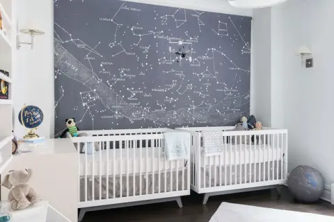 Two white cribs in a nursery with a constellation mural. This is a perfect example of baby boys nursery designs, inspiring dreams of the stars.