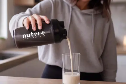 Frau gießt pflanzliches Protein aus einem Shaker in ein Glas. Informiere dich über mögliche proteinpulver nebenwirkungen.