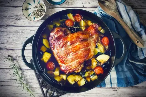Knusprige putenoberkeule im Bräter mit Gemüse, Tomaten und Kräutern.