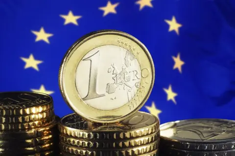 Monety euro na tle flagi UE. Pamiętasz, w którym roku weszło euro w Niemczech?