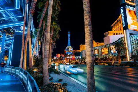 Nocne Las Vegas atrakcje: palmy, neonowe światła, wieża Eiffla i ruch uliczny.