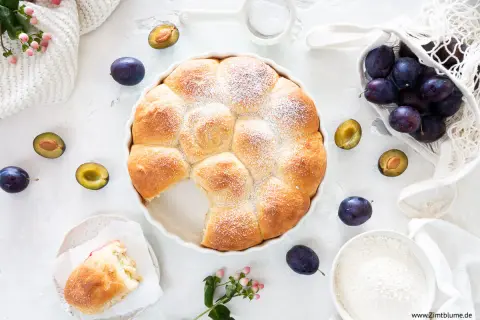 Ein goldbrauner Hefekuchen mit Puderzucker, umgeben von frischen Pflaumen. Perfekt für ein Buchty Rezept!