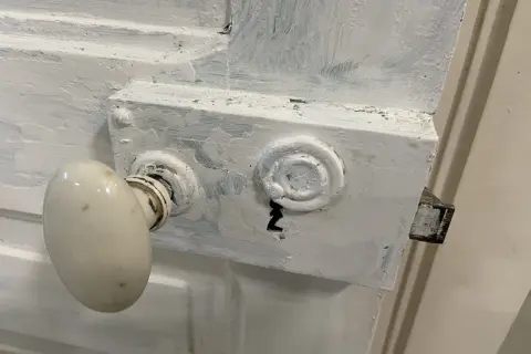 Poignée de porte ancienne recouverte de peinture blanche écaillée. Le mécanisme de serrure est visible, prêt à enlever peinture sur poignée de porte.