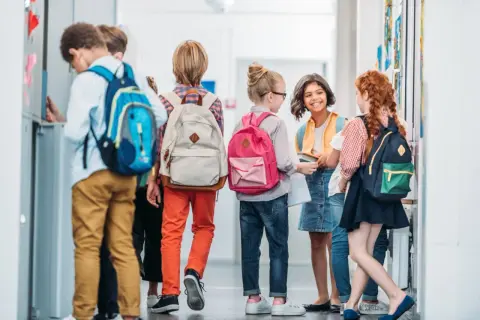 Uczennica i jej koledzy rozmawiają w szkolnym korytarzu, każdy z plecakiem gotowym na nowy dzień nauki.